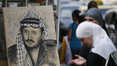 A Palestinian woman stands by a drawing of late Palestinian leader Yasser Arafat, displayed on a street corner in the West Bank city of Ramallah. The cause of his death in 2004 is once again in the spotlight after a documentary alleged that he was poisoned.