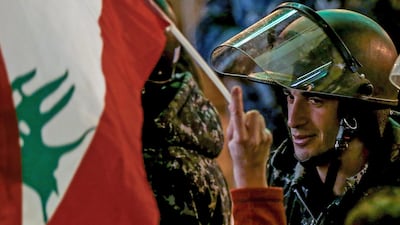 A protester waves the Lebanese flags in front of Lebanese policemen at a barricade, during an anti-government protest in front of the Parliament building in Beirut on Sunday, December 8. EPA