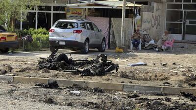People sit near the scene of a suicide attack after a suicide car bomb struck a checkpoint in the eastern suburb of Hussainiyah, Baghdad, Iraq. Suicide attacks targeting security forces in two Baghdad suburbs have killed and wounded dozens of people. Karim Kadim / AP
