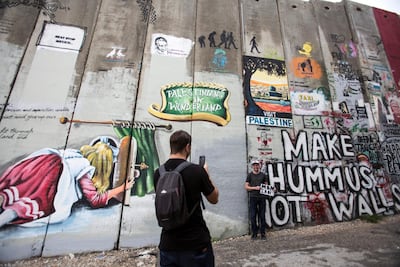 A Canadian tourist poses with a sign telling his mother he is okay as he stands against the 8 meter high separation wall built by Israel that is next to Bansky's Walled Off Hotel in the Palestinian city of Bethlehem on November 24,2018.The barrier wall has become a giant canvas of artistic resistance .(Photo by Heidi Levine for The National).