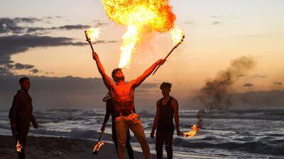 A Palestinian performer in Gaza city blows a cloud of flame on the beach, where spectators gather and sand serves as a damper of flames.