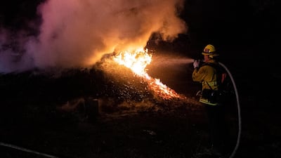 A firefighter extinguishes a brush fire lit by the Tick Fire in the hills next to a factory near Santa Clarita. EPA