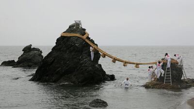 Japanese Shinto shrine priests hang the Shimenawa, Sacred ropes between God Married Stones during the Oshimenawahari ceremony of Meoto-iwa or the Couple Rock at Futami Okitama Shrine in Ise, Japan. The Oshimenawahari ceremony is held three times a year to exchange the heavy rope of rice straw that connects the Couple Rock. The Couple Rock serves as a gate to the Okitama Shrine, dedicated to the god Sarutahiko and goddess Ukanomitama from Japanese myth. Buddhika Weerasinghe / Getty Images