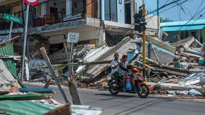 Motorists ride past buildings ruined by an earthquake in Lombok, Indonesia. AP