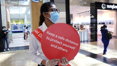 A woman wearing a protective face mask and gloves holds a sign at Mall of the Emirates. The Philippine labour office was closed for two days in Dubai after a suspected outbreak of the virus. Reuters