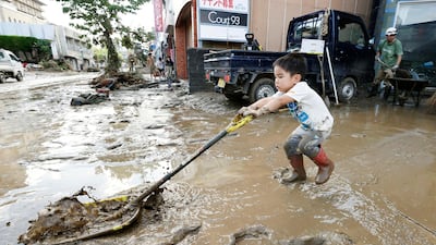 A boy helps to clear dirt in front of his grandparents' house following a heavy rain in Hitoyoshi, Kumamoto prefecture, southern Japan on July 4, 2020. Kyodo News via AP
