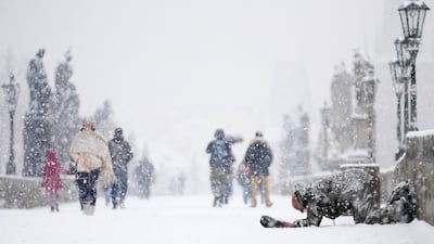 A beggar kneels at the medieval Charles Bridge as snow falls in Prague, Czech Republic, Friday, March 4, 2022. (AP Photo / Petr David Josek)