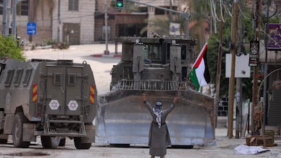 A man raises a Palestinian flag and flashes the victory sign as Israeli armoured vehicles drive on a street during a raid in Tulkarm. AFP