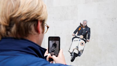 A person takes a photo of a mural depicting new AS Roma coach Jose Mourinho riding a Vespa on a wall in Rome. Reuters