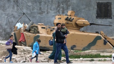A family walks past a military vehicle belonging to Turkish-backed Free Syrian Army fighters after the capture of Khaldieh village, in eastern Afrin, Syria on March 10, 2018. Khalil Ashawi / Reuters