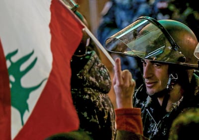 A protester waves the Lebanese flag in front of policemen at a barricade, during an anti-government protest in front of the Parliament building in Beirut, Lebanon, December 8, 2019. EPA / NABIL MOUNZER