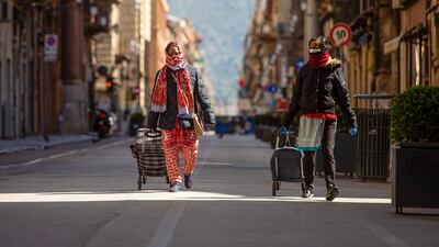 Pedestrians pull trolley bags along a nearly deserted street in Palermo, Italy. Bloomberg