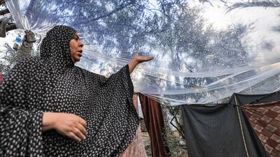 A Palestinian woman stands under a plastic sheet spread to shelter from the rain. AFP