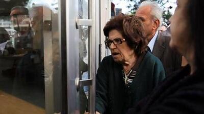 A woman holds the door of a Laiki bank branch in the Cypriot capital, Nicosia yesterday as people queue up outside waiting for the bank to open after an unprecedented 12-day lockdown.