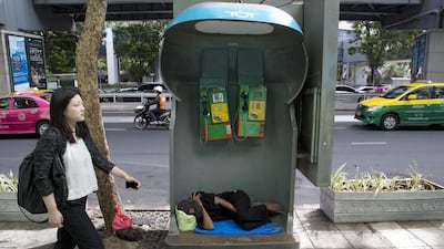 A morning commuter walks past a man sleeping in a phone booth in central Bangkok. The Social Development and Human Security Ministry said in a 2015 report the number of homeless people and beggars in Bangkok had risen by 5-10 per cent on a yearly basis since 2012. Mark Baker / AP