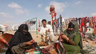 Ghariba Mohammed, left, and Umm Mahmoud, right, sew traditional fabric camel bling while Mohammed Asaif, center, looks to try to sell his shiny, plastic beads at the Al Dhafra Festival outside Abu Dhabi.