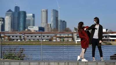 People wearing face masks as a precautionary measure against covid-19 'elbow bump' as they stand in Greenwich in south London. AFP