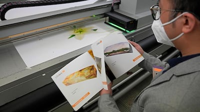 Mr Tong looks at a catalogue showing more than 40 different choices of coffin designs as a machine prints the lily design.