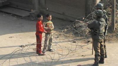 Kashmiri children ask Indian paramilitary soldiers permission to cross barbed wire set up as a road block on the fourth consecutive day of a curfew imposed after the execution of a Kashmiri man.