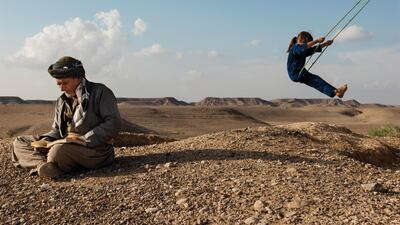 KOLOJO, IRAQ: Rostam Haji Hamajan reads the Quran while a girl plays on a rope swing.
