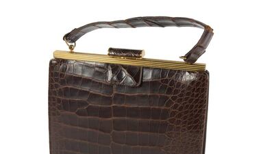 A chocolate brown 1950s alligator handbag features gold metal hardware and burgundy leather interior with purpose-built pockets to accommodate matching accessories. Courtesy Julien's Auctions