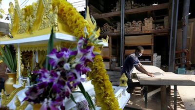 A Thai wood worker cuts planks of shipping pallet wood to size, near a Thai spirit house covered in flower offerings close to Bangkok's Klong Toey port. But change is coming. The crapentry business community here is trespassing, according to the Bangkok Port Authority, who want the land back. Barbara Walton / EPA
