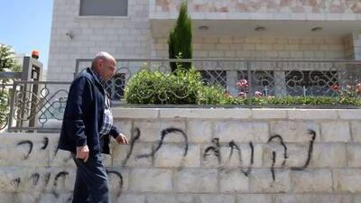 A Palestinian man walks past graffiti painted on a wall outside a house in Hebrew reading "price tag" near where two vehicles were torched in the east Jerusalem neighborhood of Sheikh Jarrah.