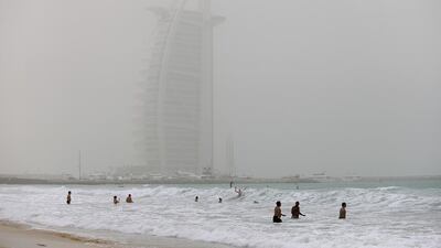 Beachgoers enjoy the cool water at Umm Suqiem Beach as the Burj Al Arab is cloaked in dust in Dubai, March 16, 2014. Sarah Dea / The National