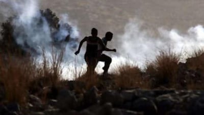 Palestinian protestors carrying sling shots run as tear gas curls behind them during a demonstration against Israel's controversial separation barrier in the West Bank village of Nilin.