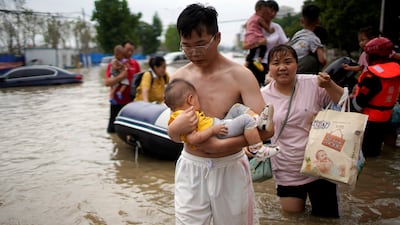 A man holding a baby wades through a flooded road in Zhengzhou.