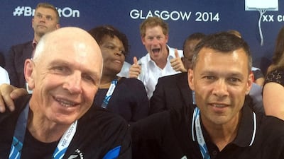 New Zealand representatives Sir Gordon Tietjens, left, and Trevor Shailer, as they pose for a photo while a Britain’s Prince Harry, centre rear, gives the thumbs up and smiles while they watch the swimming at the Tollcross International Swimming Centre, during the 2014 Commonwealth Games in Glasgow Scotland. AP Photo
