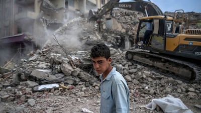 A young man walks past as diggers work to clean the rubble of collapsed buildings in Turkey in July, several months after a 7. 8-magnitude earthquake devastated the country and neighbouring Syria. AFP