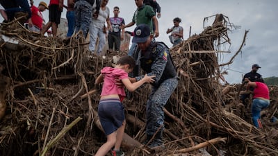 A policeman helps a child in Tejerias after a month's worth of rain fell in eight hours. EPA