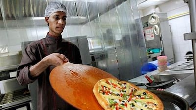 A cook slides a pizza onto a serving plate in the kitchen at a Pizza Hut restaurant in Mumbai, March 29, 2011. A number of fast-food and cafe chains that are flocking to India would do well to take away lessons learned by established rivals such as McDonald's in navigating a market beset with obstacles. Industry experts say patience and flexibility in a country where dietary traditions rule may well define successful global restaurant brands in India. The stakes are high, with India's quick-service restaurant market worth $13 billion and growing roughly 25-30 percent a year, according to Euromonitor and market research firm RNCOS. India's entire food-service market is estimated at $64 billion. Picture taken March 29, 2011. To match analysis INDIA-FASTFOOD/ REUTERS/Danish Siddiqui (INDIA - Tags: BUSINESS FOOD)