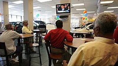 Car salesmen and customers gather to watch Barack Obama comment on General Motors. The company has effectively been nationalised by its recent bailouts.