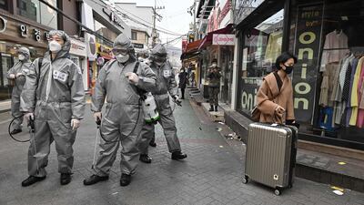 A woman walks past South Korean soldiers wearing protective gear as they spray disinfectant to help prevent the spread of the virus. AFP
