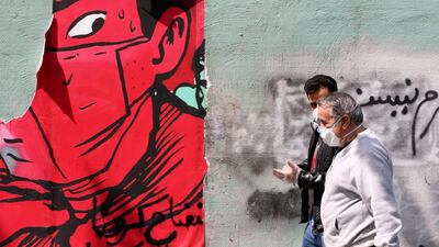 Iranians wearing protective mask walk past graffiti on a wall in Tehran. AFP