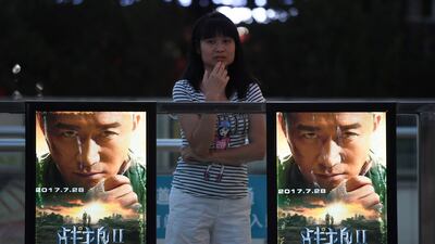 A woman stands next to posters for the film Wolf Warrior 2 in Beijing on August 7, 2017. Greg Baker / AFP