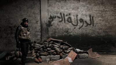 A National Security Service officer stands next to a pile of mortar rounds stashed under an ISIL scrawl in an abandonned warehouse in east Mosul. (Florian Neuhof for The National)
