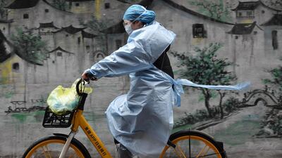 A woman in protective gear rides a shared bicycle past a mural in Wuhan, the epicentre of the novel coronavirus outbreak, Hubei province, China. Reuters
