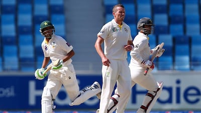 Pakistani batsmen Ahmed Shahzad, right, and Younis Khan run between wickets as Australian bowler Peter Siddle, centre, looks on during the fourth day of the first Test at Dubai International Cricket Stadium in Dubai on October 25, 2014. Marwan Naamani / AFP