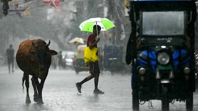 Commuters cross the street during rainfall in New Delhi. AFP