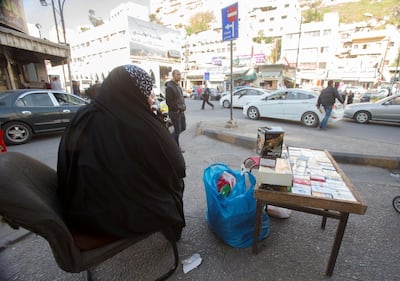 Iraqi refugee Um Saad sits on the sidewalk of a street selling cigarettes in Amman, Jordan. (Salah Malkawi for The National)