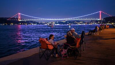 People enjoy the evening as they sit next to the shore of the Bosphorus as Fatih Sultan Mehmet bridge is seen in the backround in Istanbul. AFP