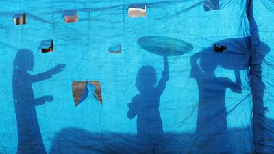The silhouettes of Iraqi refugee children are seen on tarpaulin as they collect water at the Al Khazir camp located between Erbil and Mosul. Karim Sahib / AFP Photo