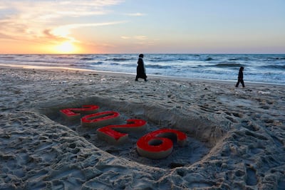 Palestinians walk past a sand sculpture on the beach in Gaza city marking the new year. AFP