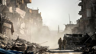 This photo taken on October 20, 2017 shows fighters of the Syrian Democratic Forces (SDF) walking down a street in Raqqa past destroyed vehicles and heavily damaged buildings after a Kurdish-led force expelled ISIL fighters from the northern Syrian city, formerly their "capital". Bulent Kilic / AFP
