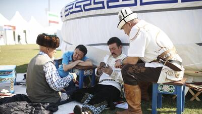 Falconers from Kazakhstan and Mongolia sit beside a yurt.