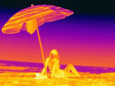 Thermal image rear view of young woman sitting on beach underneath umbrella. Getty Images