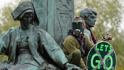 A climate activist climbs a statue during the protest in the centre of Glasgow. AP Photo